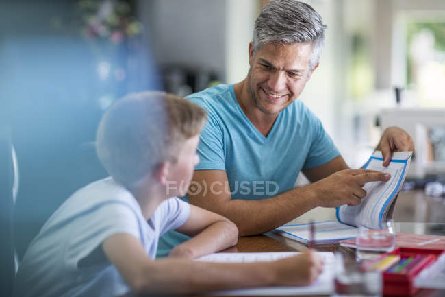 Pai feliz e filho lendo livro juntos à mesa, escola em casa — Fotografia de Stock