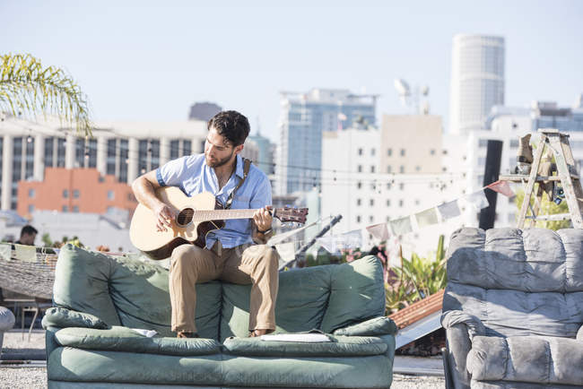 Man playing guitar at rooftop party, Los Angeles view on background, USA — Stock Photo