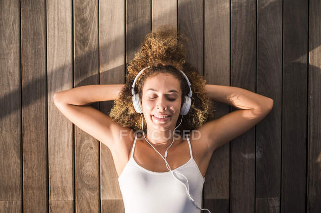 Portrait de jeune femme les yeux fermés couché sur le sol en bois et écoutant de la musique avec écouteurs — Photo de stock