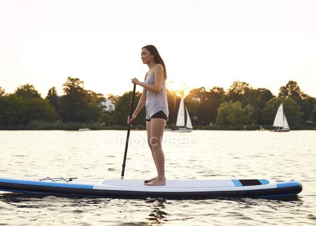 Jeune femme sur planche à pagaie profitant du coucher de soleil d'été — Photo de stock