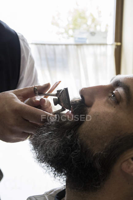 Barber cutting man beard in barbershop saloon — Stock Photo
