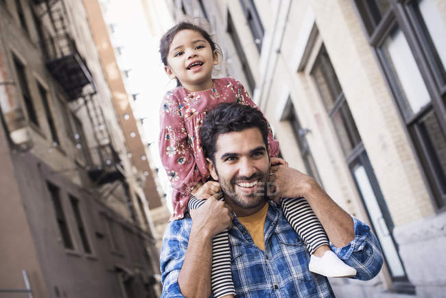 Glücklicher Vater trägt Tochter auf Schultern, die durch die Straße läuft — Stockfoto