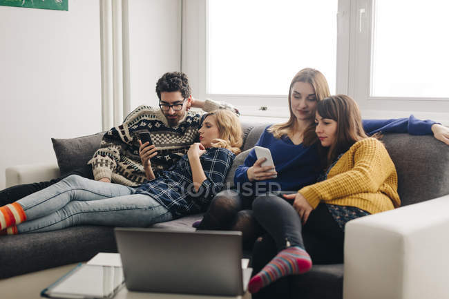 Чотирьох друзів з смартфонами на канапі у вітальні, проведення часу — стокове фото