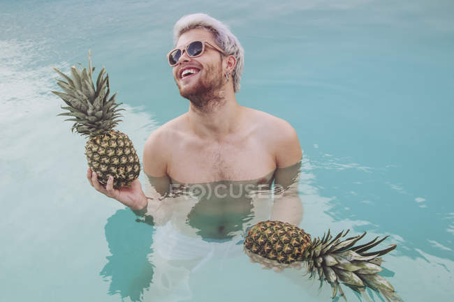 Усміхнений молодий чоловік тримає ананаси в басейні — стокове фото