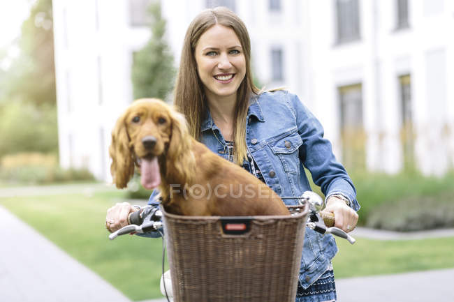 Smiling woman with dog in bicycle basket — Stock Photo