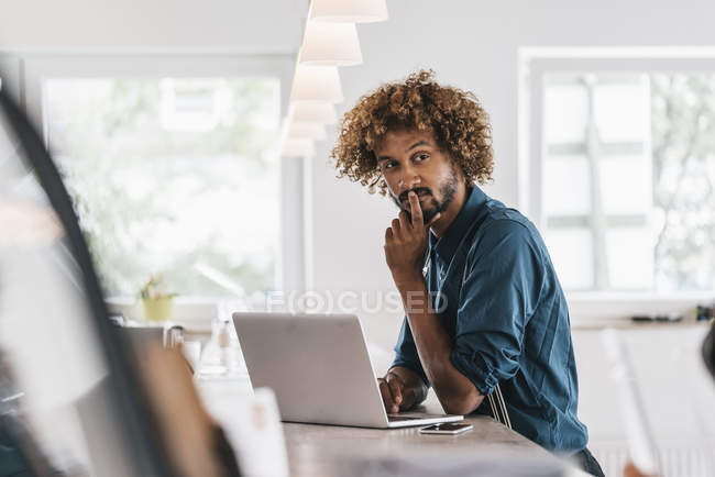 Jeune homme avec coiffure afro en utilisant un ordinateur portable dans un bureau moderne — Photo de stock