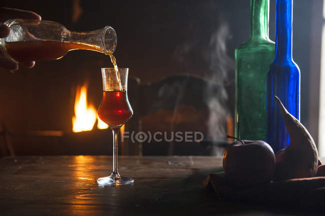 Mano vertiendo licor en vaso de chupito en frente de fuego abierto - foto de stock