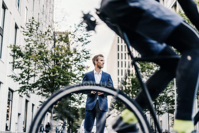 Велосипедист на улице в городе с бизнесменом на заднем плане — стоковое фото