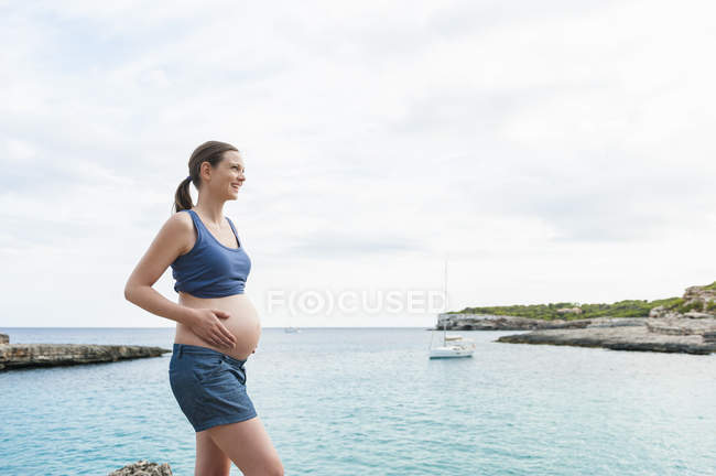 Sonriendo mujer embarazada caminando en el mar - foto de stock