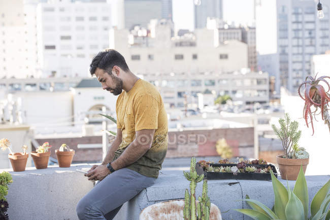 Hombre con teléfono inteligente sentado en la fiesta en la azotea, Los Ángeles, Estados Unidos - foto de stock