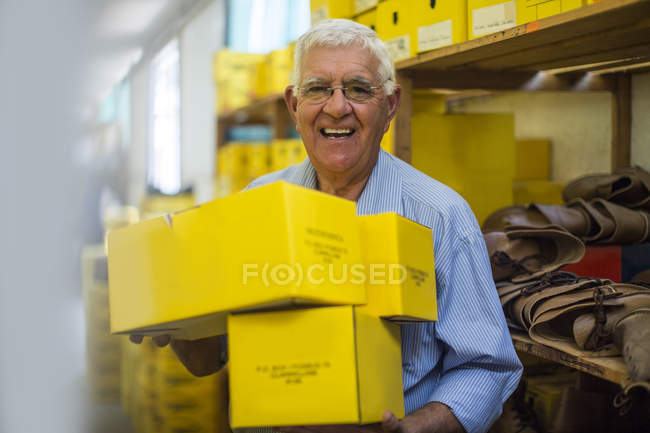 Uomo anziano sorridente in magazzino che trasporta scatole di scarpe — Foto stock