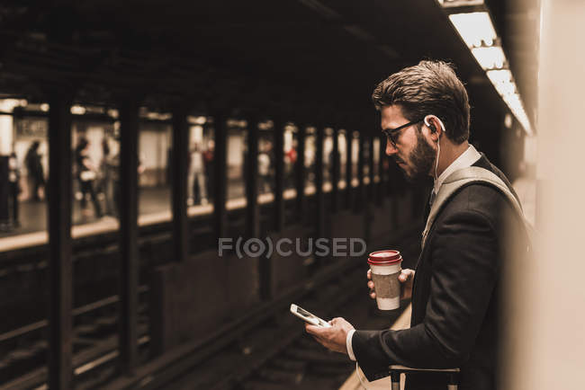 Junger Geschäftsmann wartet mit Smartphone am Bahnsteig der U-Bahn — Stockfoto