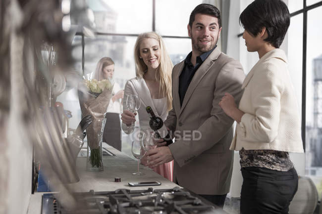 Uomo con amiche e bottiglia di vino in cucina — Foto stock