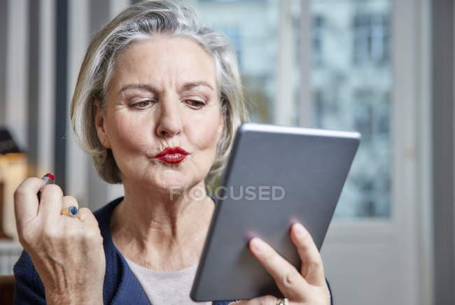 Seniorin trägt Lippenstift mit Tablette auf — Stockfoto