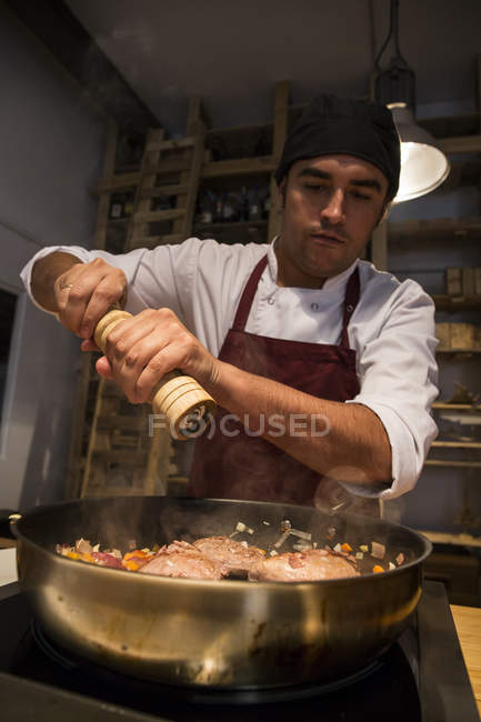 Man pouring pepper on beef cheeks in pan with sauteed vegetables — Stock Photo