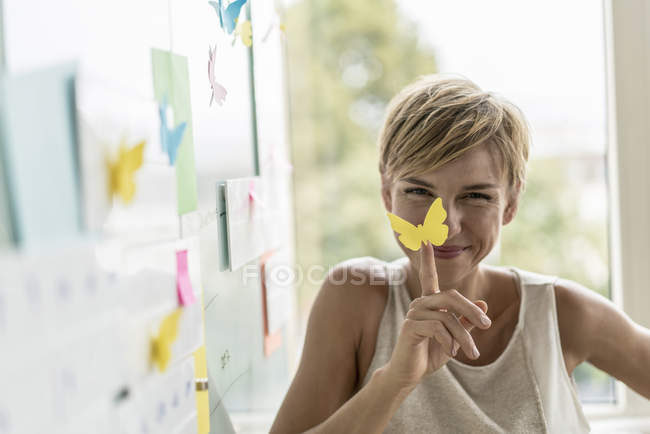 Femme d'affaires souriante assise avec des notes adhésives au tableau blanc dans un bureau moderne — Photo de stock