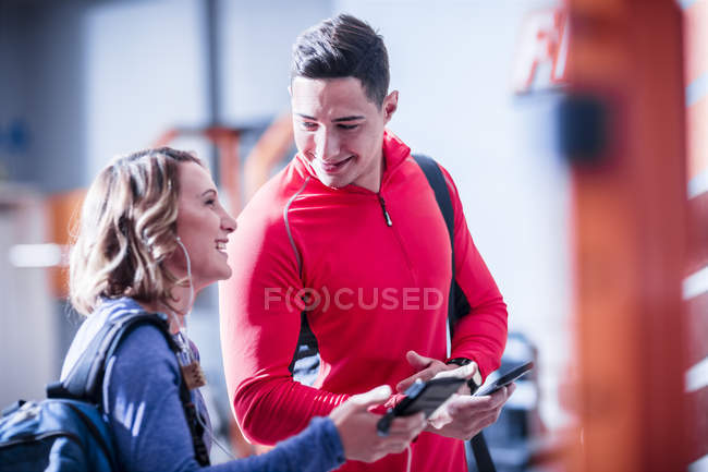 Young man and woman with cell phones and earbuds in gym — Stock Photo