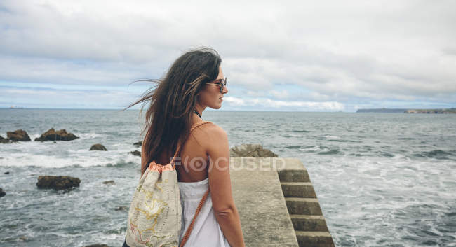 Mujer con mochila de pie en el muelle y mirando a la distancia - foto de stock