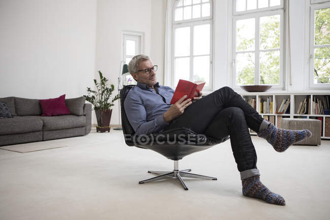 Mature man sitting in chair at home and reading book — Stock Photo