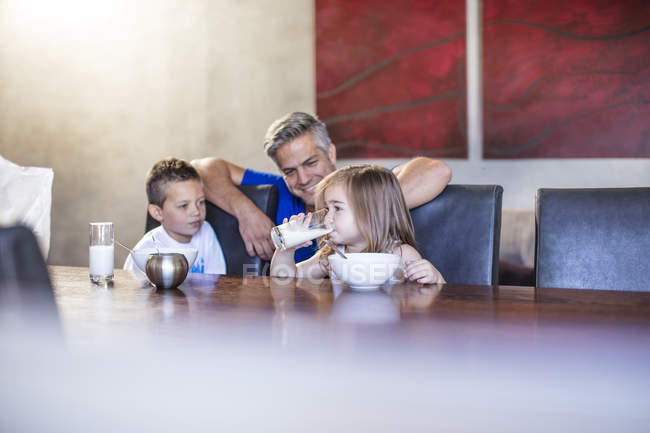 Pai feliz com crianças sentadas tomando café da manhã à mesa — Fotografia de Stock