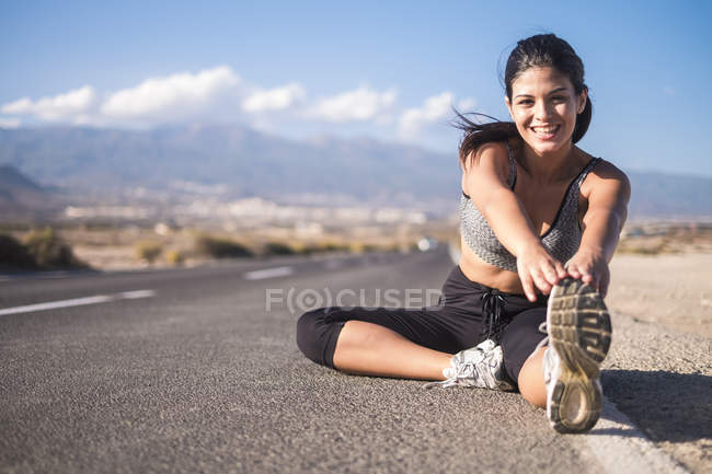 Jeune femme faisant des exercices d'étirement sur la route vide — Photo de stock