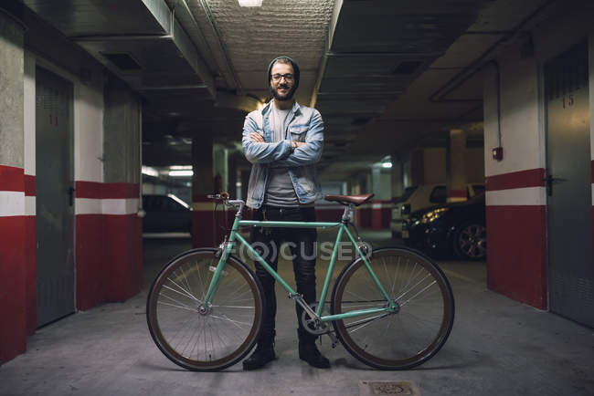 Случайный молодой человек, стоящий возле своего велосипеда в гараже — стоковое фото