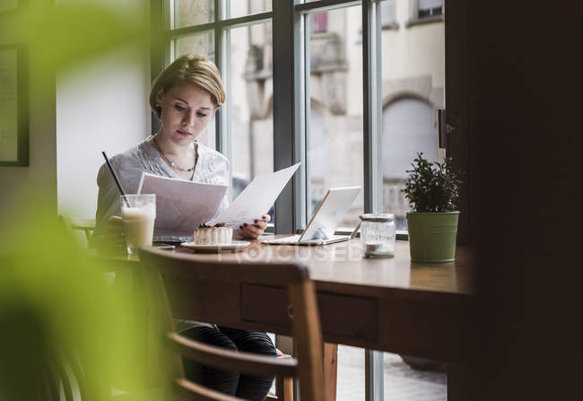 Young woman with documents and tablet sitting in a cafe — Stock Photo