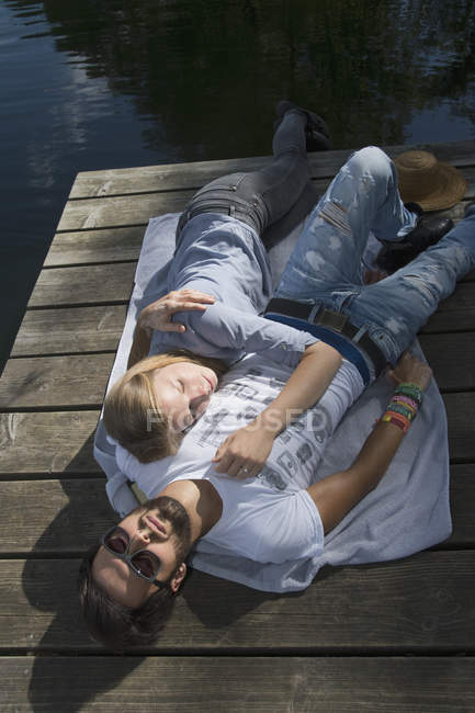 Relajada joven pareja acostada en el embarcadero en un lago - foto de stock