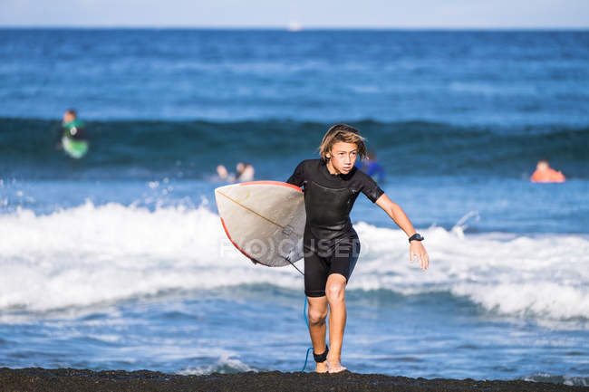 Spain, Tenerife, boy carrying surfboard at sea — Stock Photo