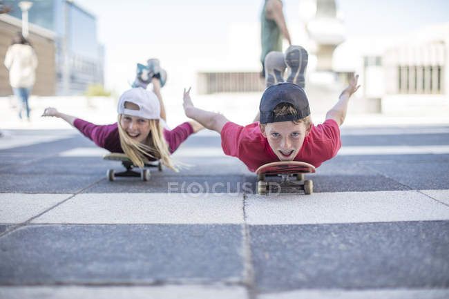 Portrait of smiling Kids skateboarding on street, lying on belly — Stock Photo