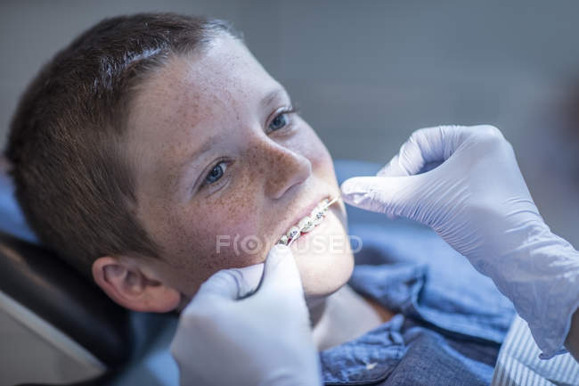 Niño con aparatos ortopédicos en cirugía dental que recibe tratamiento con hilo dental - foto de stock