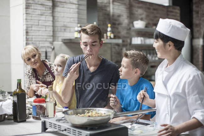 Adolescent mâle goûte en toute confiance des aliments bien cuits avec ses frères et sœurs en cours de cuisine — Photo de stock