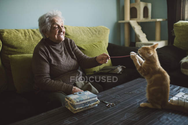 Glückliche Seniorin spielt zu Hause mit Ingwerkätzchen — Stockfoto