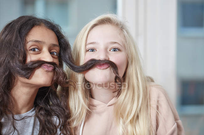 Портрет двох грайливих дівчат, які вдають, що мають вуса з волосся — стокове фото
