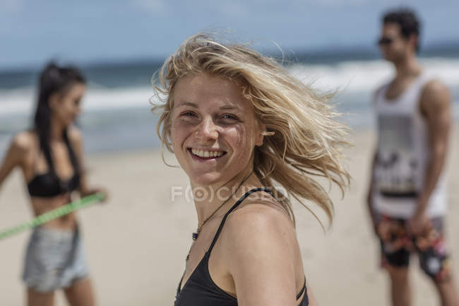 Happy young woman on the beach with friends in background — Stock Photo