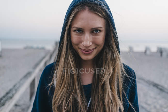 Portrait of smiling young woman wearing hooden jacket standing on jetty — Stock Photo