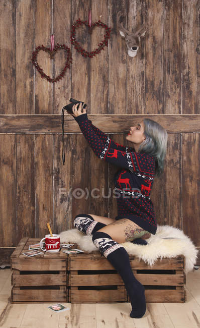 Молодая женщина в узорчатом вязаном свитере и накладывающихся коленях делает селфи с помощью поляроидной камеры — стоковое фото