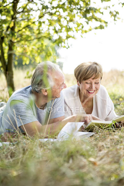Старший пару, що лежить на відкритому повітрі у сонячному саду з книгами — стокове фото