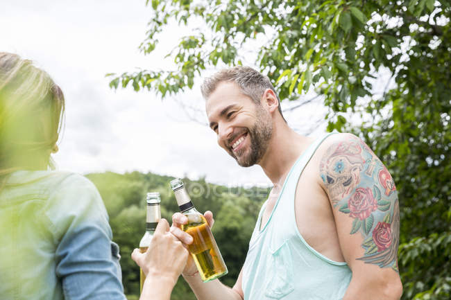 Усміхаючись пара дзвінкою пляшок пива в природі — стокове фото