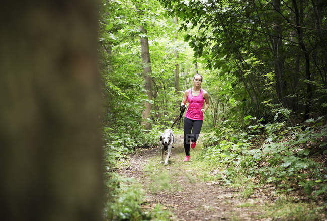 Junge Frau joggt mit Hund im Wald — Stockfoto