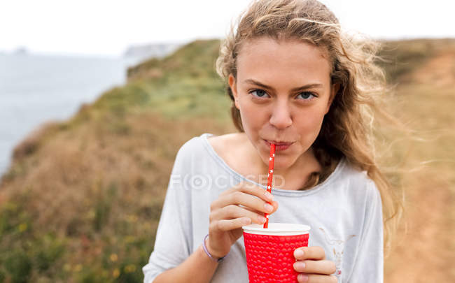 Portrait of teenage girl with beverage standing at the coast — Stock Photo