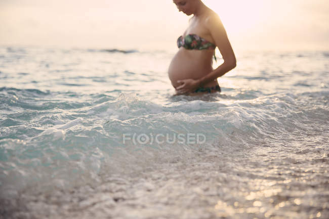 Donna incinta in piedi nel mare alla retroilluminazione — Foto stock