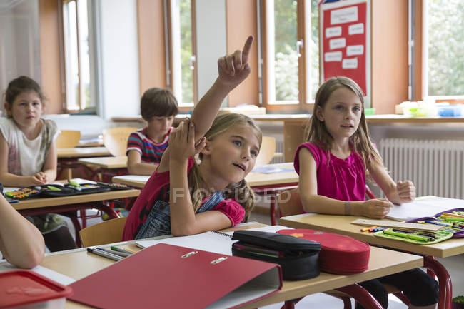 Schoolgirl raising her hand in class at school — Stock Photo
