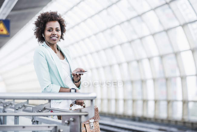 Woman with earphones and smartphone waiting at platform — Stock Photo