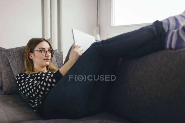 Jovem relaxante no sofá com seu tablet — Fotografia de Stock