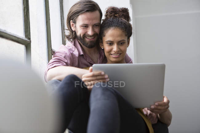 Jeune couple assis sur le rebord de la fenêtre en utilisant un ordinateur portable — Photo de stock