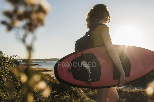 Ragazza adolescente sulla spiaggia che trasporta tavola da surf — Foto stock