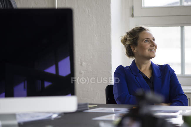 Empresária sentada no cargo com os braços cruzados, sorrindo — Fotografia de Stock
