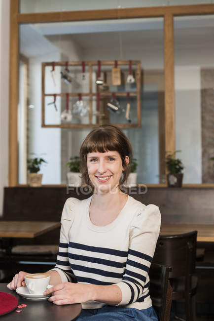 Retrato de mulher sorridente sentada em um café com xícara de café — Fotografia de Stock