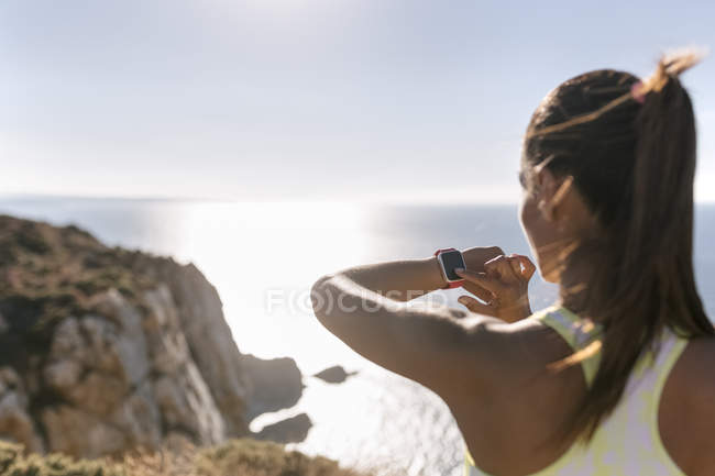Spain, Asturias, sportswoman on the coast, looking at the smartwatch — Stock Photo
